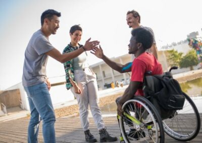 Un jeune en fauteuil roulant rit avec d'autres jeunes debout et tape dans les mains d'un d'entre eux