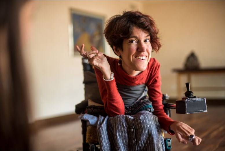 une dame atteinte d'ostéogenèse imparfaite sourit dans son fauteuil
