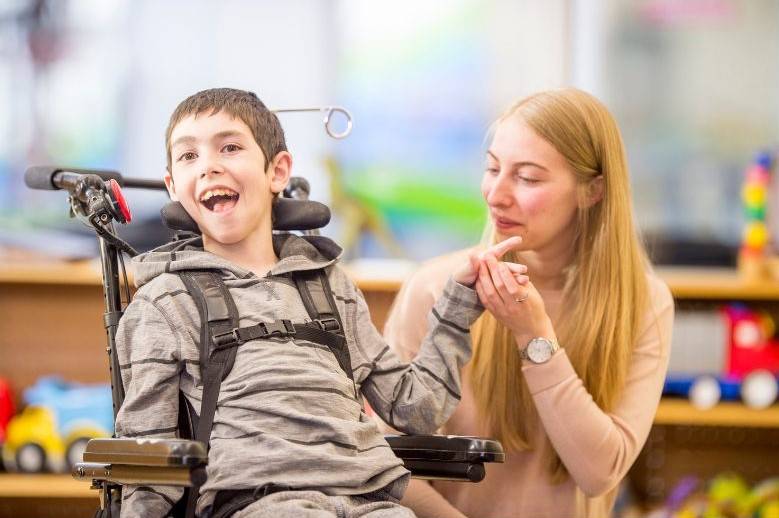 un enfant en situation de polyhandicap sourit une dame lui tient la main